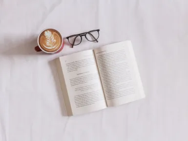 Une paire de lunettes posée près d'un café et d'un livre ouvert.